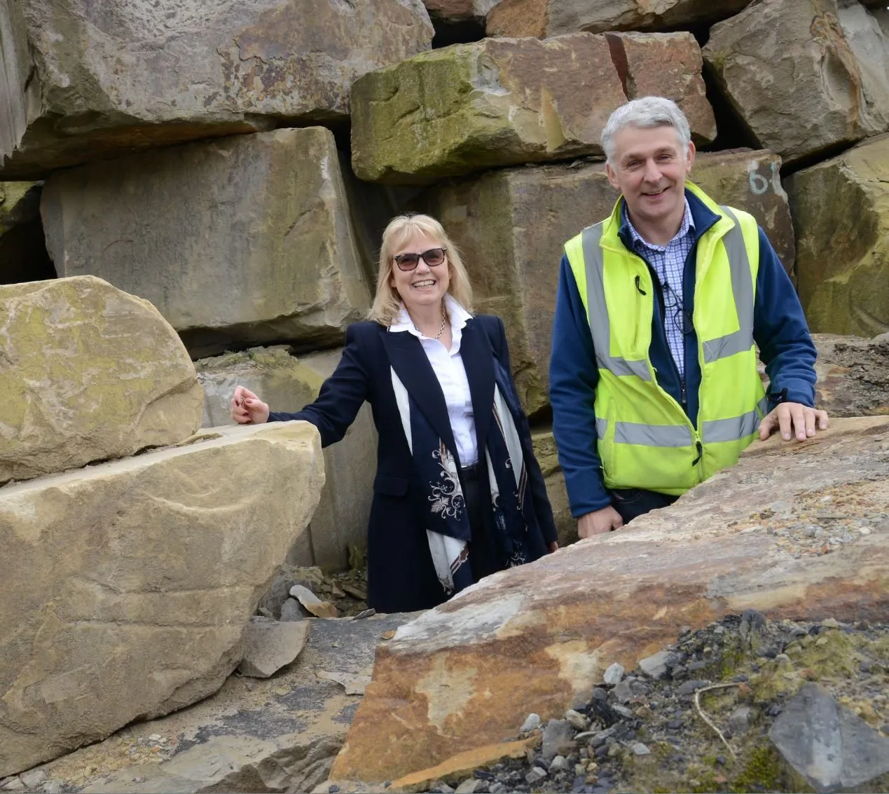 A man in a high-visibility vest and a woman standing among large blocks of cut sandstone at Dunhouse Quarry