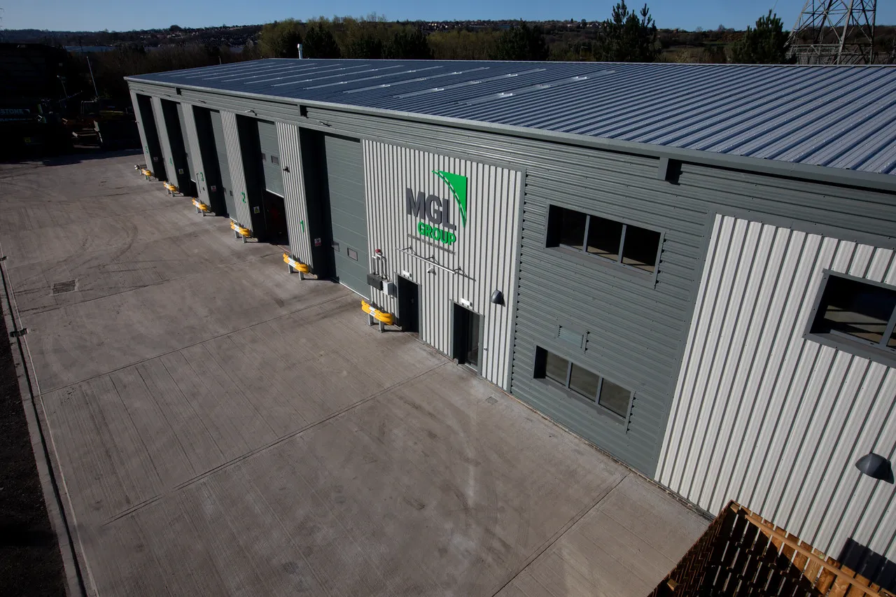 MGL Group's grey and white industrial unit with a row of roller shutter loading doors and the green MGL Group logo, seen from above across an empty concrete yard