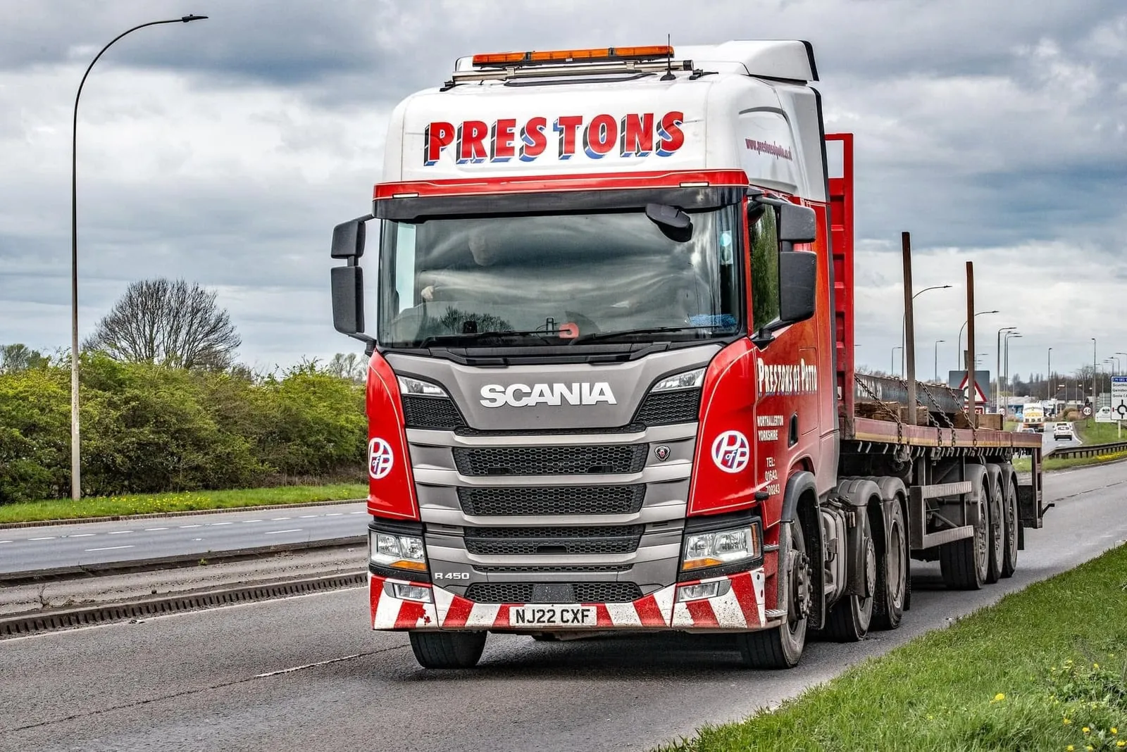 A red and white Prestons of Potto Scania lorry with a flatbed trailer on a dual carriageway