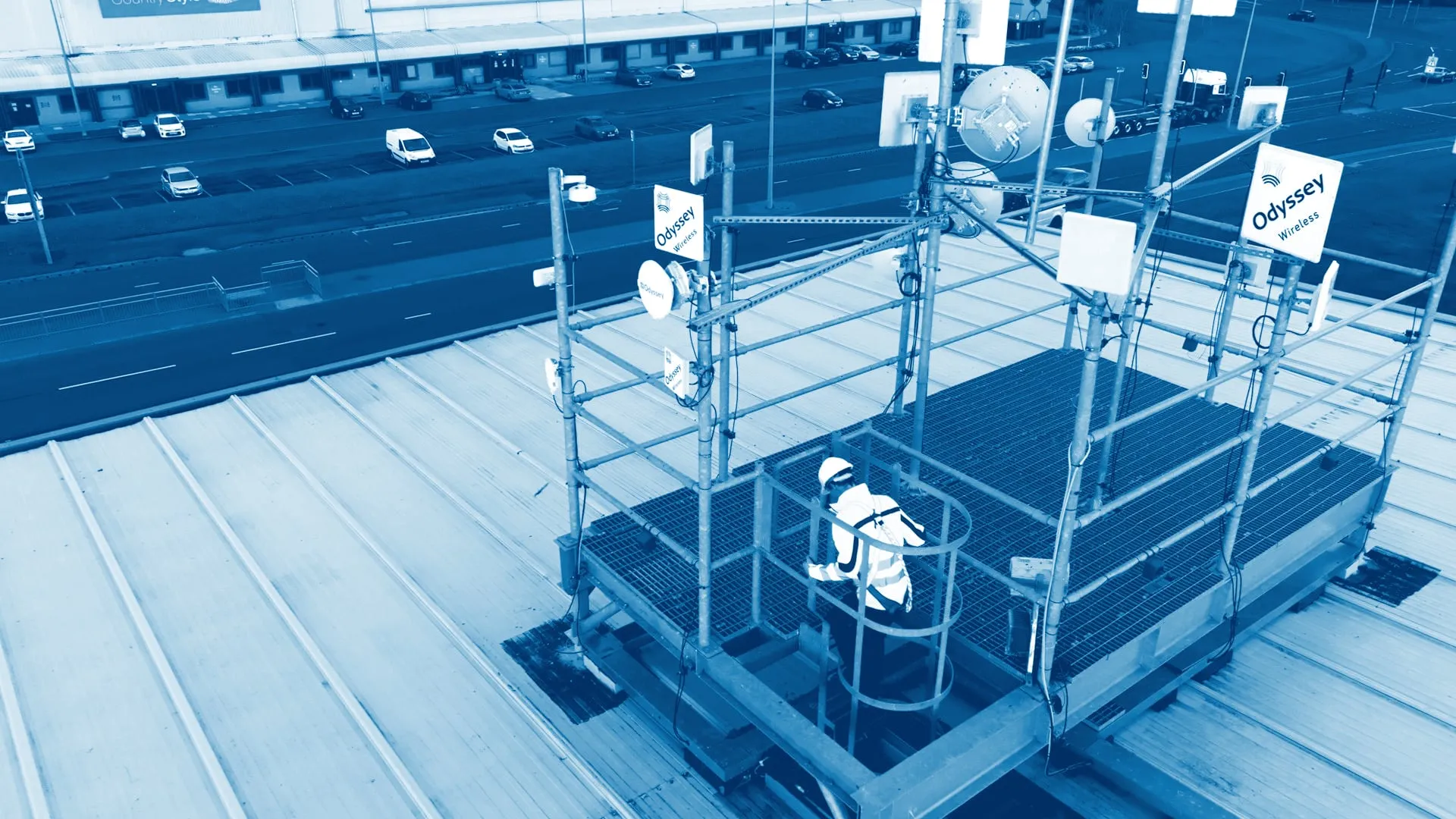 An engineer in a harness on a rooftop mast platform carrying Odyssey Wireless antennas