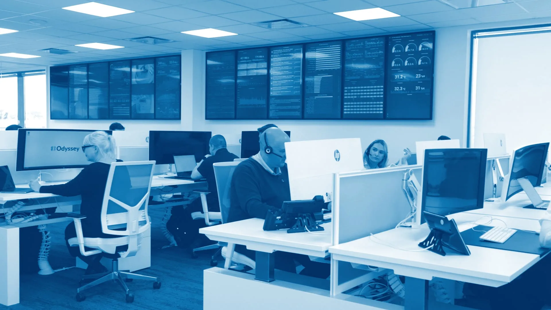 The Odyssey service desk: the team at their desks, some on calls, beneath a wall of network monitoring screens